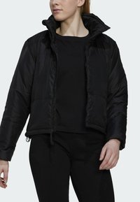 Zwarte puffy jas met een hoge kraag, ritsluiting en verstelbare koordjes aan de onderrand. Gladde textuur en lichtgewicht ontwerp.