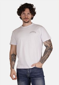 T-shirt bianco in cotone con una piccola stampa "PROPAGANDA" grigia sul lato sinistro del petto. Maniche corte e design classico con colletto rotondo.