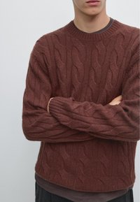 Trui met kabelpatroon in roestkleur, gemaakt van gestructureerde stof. Heeft een ronde hals, geribbelde manchetten en een losse pasvorm.