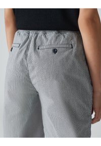 Striped gray fabric trousers with an elastic waistband, back pockets with buttons, and a smooth texture. Subtle vertical lines pattern.