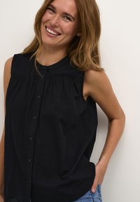 Top senza maniche nero con chiusura a bottoni sul davanti, tessuto morbido e design plissettato, con scollatura rotonda e vestibilità comoda.