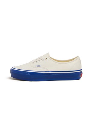 Baskets en toile crème avec une semelle en caoutchouc bleue. Caractéristiques de coutures et de lacets blancs, avec un logo Vans sur le côté. Design basse.