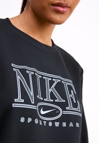 Svart sweatshirt med en stor vit Nike-grafiklogga och texten "SPORTSWEAR" nedanför. Klassisk crewneck-design och mjuk textur.