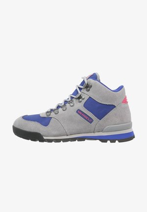 Botte de randonnée en daim gris avec des accents en tissu bleu, semelle en caoutchouc noire, six œillets métalliques et un détail de logo rouge sur le côté.