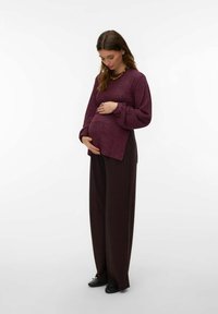 Porodniški pulover v bordo pletenini z dolgimi rokavi, kombiniran s temnimi, širokimi plisiranimi hlačami, ki ustvarjajo sproščen silhueto.