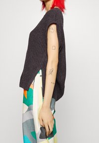 Suéter de punto gris oscuro con mangas cortas y aberturas laterales. Combinado con pantalones de pierna ancha de patrón multicolor que presentan diseños geométricos.