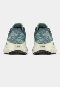 Αθλητικά παπούτσια με υφασμάτινη επάνω επιφάνεια στο χρώμα του πετρόλ, σκούρες μπλε λεπτομέρειες και μαξιλαρωμένη ελαφριά κρεμ σόλα. Διαθέτουν το λογότυπο της μάρκας και ετικέτα με αφρό ενέργειας στη φτέρνα.