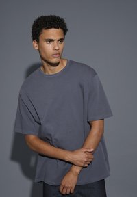 T-shirt grigio in cotone con vestibilità rilassata, maniche corte e scollatura rotonda. Presenta cuciture minime e un'etichetta del marchio discreta sull'orlo.