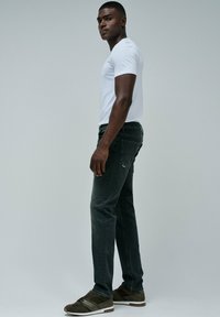Jeans grigio scuro a vita slim, abbinati a una maglietta bianca aderente e scarpe da ginnastica verdi. Il materiale sembra cotone con lievi segni di usura.