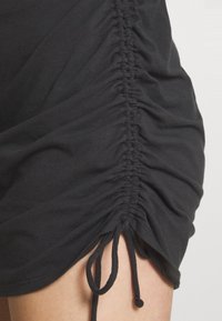 Czarna sukienka z marszczonym materiałem po bokach, z regulowanym sznurkiem u dołu, który umożliwia dostosowanie fasonu. Wykonana z miękkiej bawełny.