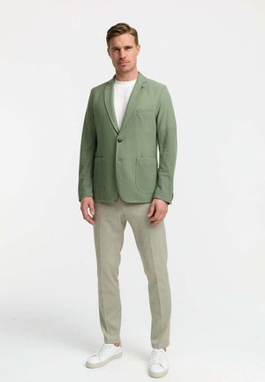 Light green, textured blazer with two front pockets, single button closure, and lapels. Paired with light beige trousers and white sneakers.