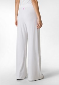 Valkoiset leveälahkeiset housut, joissa on sileä ja kevyt kangas. Ominaisuuksiin kuuluu pehmeä vyötärönauha ja pieni vaaleanpunainen etiketti takana.