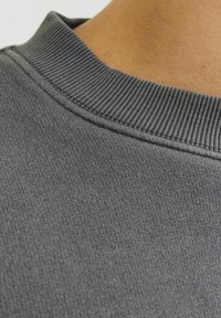 Šedá mikinová látka s texturovaným, žebrovaným límcem. Měkký, hladký povrch s mírným leskem, zašité švy jsou viditelné poblíž límce.