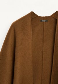 Brun kappa med sjalkrage tillverkad av mjukt, texturerat tyg, med öppen framsida och inga synliga stängningar, samt en minimalistisk design.