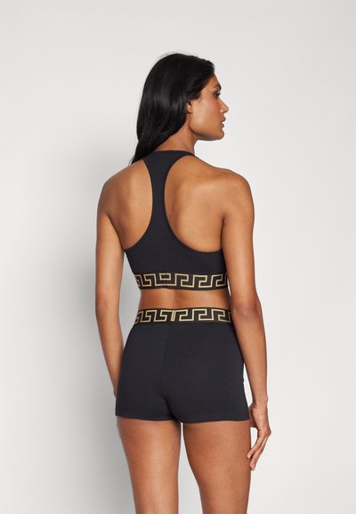 Schwarzes Sportset bestehend aus einem ärmellosen Oberteil und Shorts, verziert mit einem geometrischen goldenen Muster am Bund. Glattes, dehnbares Material.
