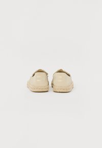 Zapatos de espadrilles beige con una parte superior de textil texturizado, suela de yute, y acento de logo en relieve en el talón. Diseñados para comodidad y uso casual.