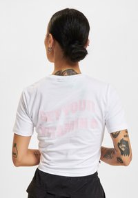 Biela krátka tričko s ružovým nápisom na zadnej strane "GET YOUR VITAMIN P." Krátke rukávy s priliehavým strihom.