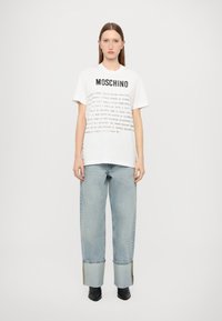 T-shirt branca da Moschino com texto preto, combinada com jeans baggy azul claro com uma bainha larga e costura em contraste. Botas pretas até o tornozelo.