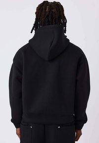 Sudadera negra con capucha y corte holgado, que presenta una capucha grande, puños acanalados y dobladillo, fabricada con un material suave y mate.