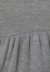 Grauer Stoff mit glatter Textur, der am unteren Rand eine geraffte Rüsche aufweist, die einen geschichteten Look erzeugt.