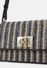 Sac à épaule avec motif tissé bleu marine et beige, bandoulière en cuir noir et fermoir argenté avec détail décoratif en forme d'arche.
