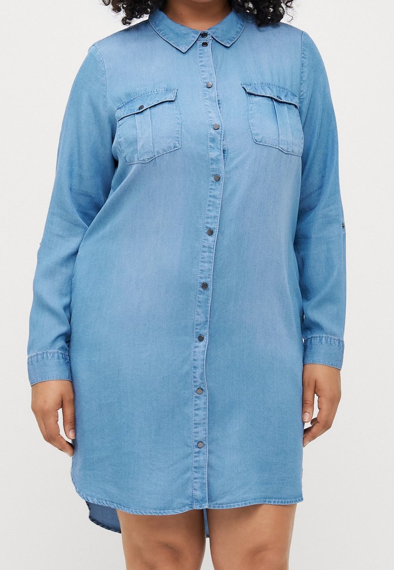 Jasnoniebieska sukienka z dżinsu, z guzikami z przodu, kołnierzykiem, dwiema kieszeniami na piersi, długimi rękawami, zaokrąglonym hemem, gładką teksturą.