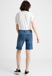 Jeansshorts i en mellanmörk blå tvätt med klassisk passform, bälteshällor och uppvikta muddkanter. Bak har de två påsydda fickor och en varumärkesetikett.