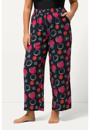 Løse sorte bukser med elastisk talje og stort rødt og pink granatæbleprint, båret barfodet med den ene hånd i lommen.