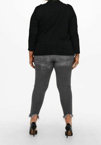 Czarny top z długim rękawem z detalami na ramionach, zestawiony z szarymi obcisłymi dżinsami z postrzępionymi nogawkami oraz czarnymi szpilkami.