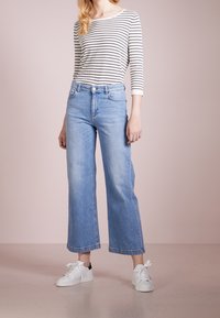 Lichtblauwe denim wijde broek met hoge taille, gestyled met een zwart-wit gestreept shirt met lange mouwen en witte sneakers.