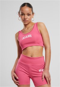 Roosa sportlik lühike topp ja vastavad püksikad, mis on valmistatud venivast kangast, millel on mõlemal osal valget värvi sõna "KANI".