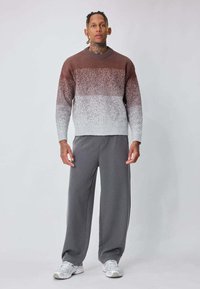 Pull en tricot dégradé marron et gris avec un col côtelé, associé à un pantalon gris ample et des baskets blanches. Design simple, texture douce.