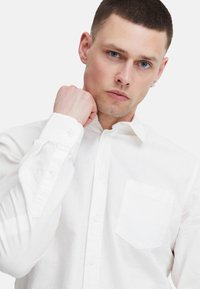 Weißes Hemd mit langen Ärmeln, Brusttasche und weicher Textur. Der Stoff wirkt leicht und atmungsaktiv, mit taillierter Passform.