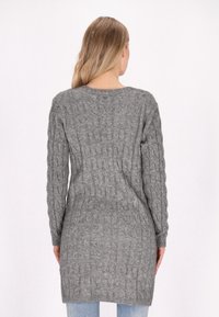 Maglione lungo grigio a intreccio con scollo rotondo, polsini a coste e superficie testurizzata. La lunghezza arriva a metà coscia.