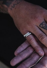 Silver ring med en dubbelbandsdesign och perforerade detaljer, visad på en hand med synliga tatueringar och hudtextur.