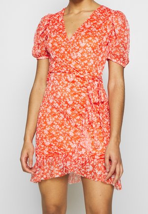 Kvinde iført en kort, orange slå-om-kjole med hvidt blomsterprint, puffede korte ærmer og flæsekant.