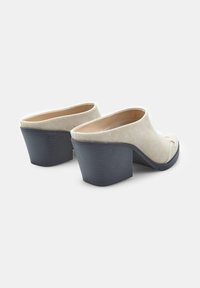Beige kanva korkulu mules, yuvarlak burun, dokulu yüzey ve sağlam siyah kauçuk topuk ile birlikte, kaydırarak giyilebilen tasarım ve dikiş detaylarıyla.