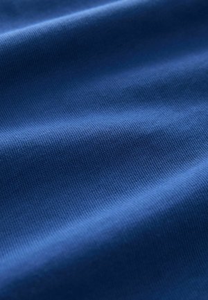 Tessuto blu con una superficie morbida e a coste, che mostra sottili variazioni di tonalità e luce attraverso le pieghe.