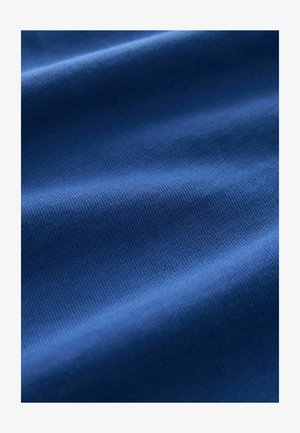 Tessuto blu con una superficie morbida e a coste, che mostra sottili variazioni di tonalità e luce attraverso le pieghe.