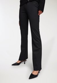 Czarne spodnie w prążki o dopasowanym kroju i delikatnym rozszerzeniu, wykonane z gładkiego materiału, połączone z czarnymi mule na obcasie w szpic.
