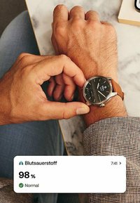 Orologio con cinturino in pelle marrone, con quadrante rotondo nero e hardware argentato, che mostra un livello di ossigeno nel sangue dell'98% e lo stato "Normale" sullo schermo.