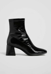 Bottine en cuir verni noir avec talon carré épais et bout pointu, vue de profil latéral sur fond gris uni.