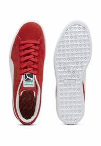 Røde ruskindsneakers med hvide gummisåler. Har kontrasterende hvide detaljer og et struktureret mønster på sålen. Puma-branding synlig.