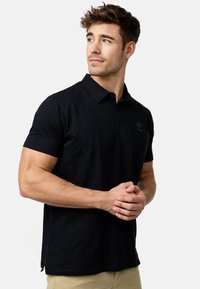 Sort polo shirt lavet af blødt stof, med klassisk krave, korte ærmer og et diskret broderet logo på brystet.