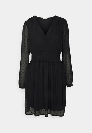 Schwarzes Langarmkleid mit durchsichtigen gepunkteten Ärmeln, V-Ausschnitt, taillierter Taille und plissiertem Rock auf schlichtem weißen Hintergrund.