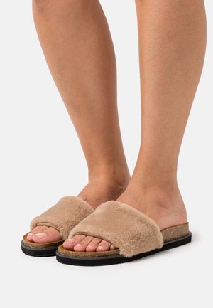 Faux-fur instap sandals in lichtbeige met een brede band, een gestructureerd oppervlak en een duurzame zwarte zool. Blootgestelde tenen zijn zichtbaar.