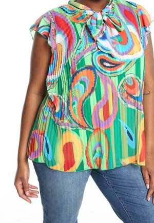 Femme portant un chemisier sans manches plissé multicolore avec des tourbillons abstraits et un col noué, associé à un jean bleu.