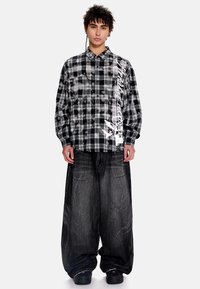 Μαύρο και άσπρο πουκάμισο με καρό μοτίβο, σε μεγάλο μέγεθος, με γιακά, που φέρει αφηρημένα σχέδια και τυπωμένο κείμενο, συνδυασμένο με σκούρο τζιν παντελόνι με φαρδιές παντελόνες.