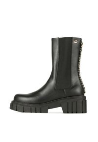 Botín negro de cuero con paneles laterales elásticos, suela plataforma gruesa y detalle decorativo de cadena en la parte trasera. Textura suave, diseño robusto.