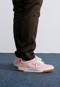 Pink sneakers med hvide detaljer, gummisål, snørebånd og en struktureret overflade. Side-logo i pink, der står i kontrast til den glatte overflade.